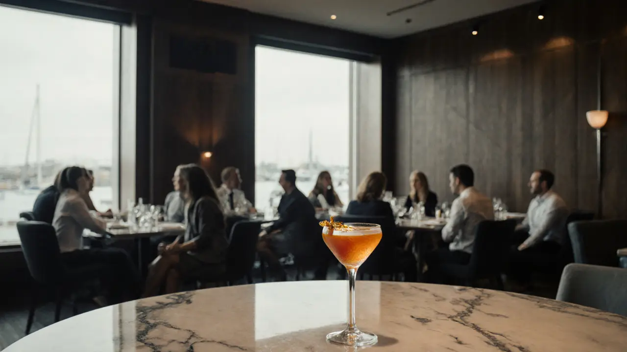 Elegant interior of La Rascasse showing dark wood tables, metal accents, floor‑to‑ceiling windows and a cocktail on the bar.